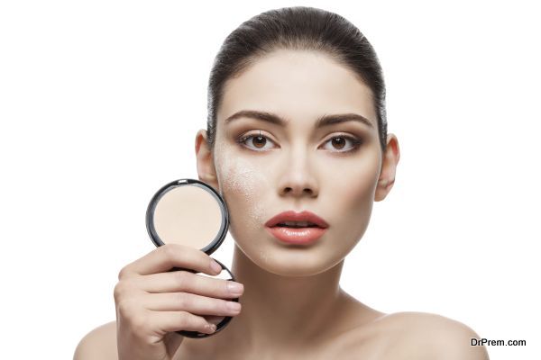 Beautiful young woman holding conrainer with pressed powder next to her face. Isolated over white background.