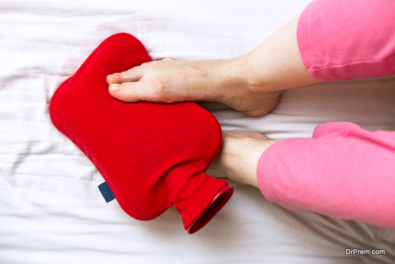 Person with cold feet in bed on a red hot water bottle